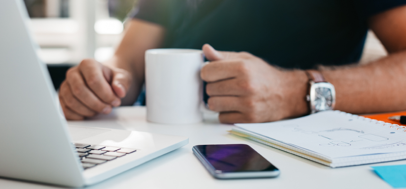 A close up of a man drink coffee with his mobile phone and laptop on desk