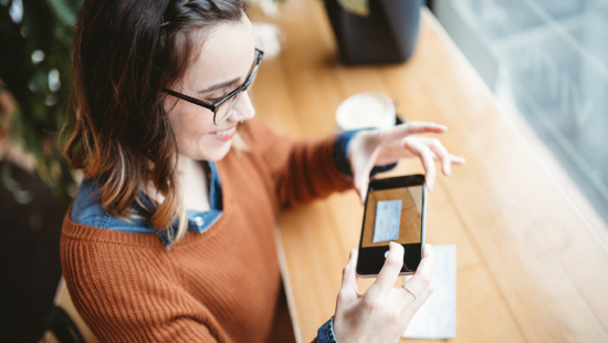 A young woman using her phone to remote deposit a check while sitting at a coffee shop