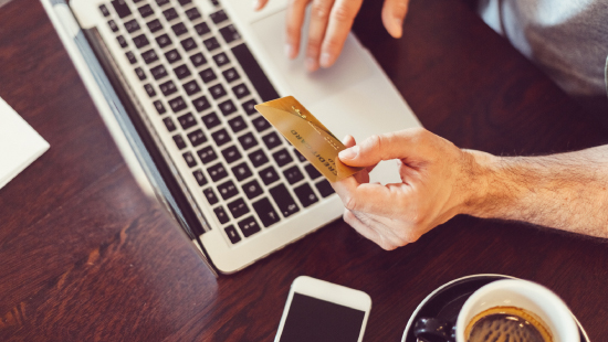 A man holding his debit/credit card while using his laptop at a coffee shop