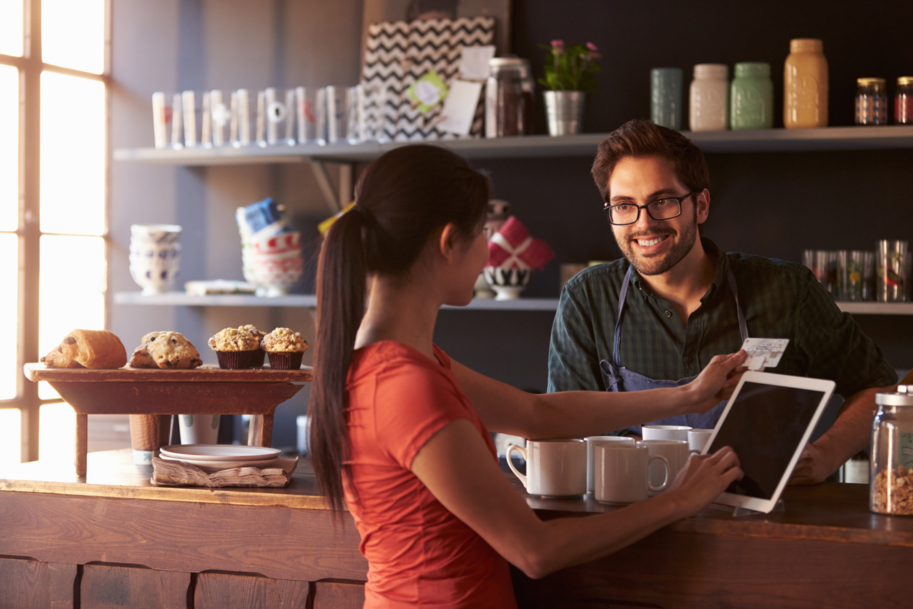 A woman uses an iPad to make a transaction at the counter of a coffee shop.
